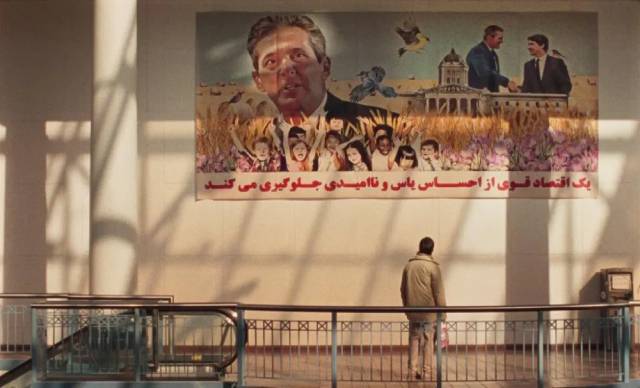 Matthew (director Matthew Rankin) pauses to look at uplifting political propaganda in the Portage Place Mall in Universal Language (2024)